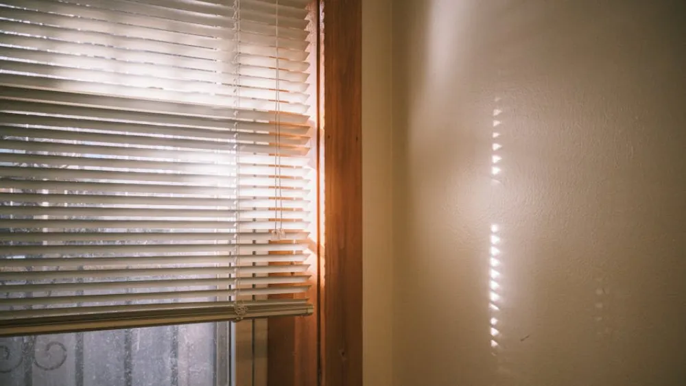 Warm sunlight casting shadows through window blinds, creating a tranquil indoor setting.